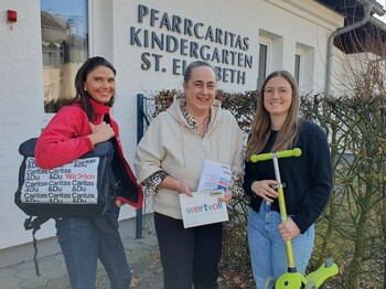 Drei Frauen stehen vor einem Kindergartengebäude und lächeln in die Kamera.