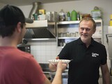 Ein Mann reicht einem anderen Mann einen Teller voll Suppe.