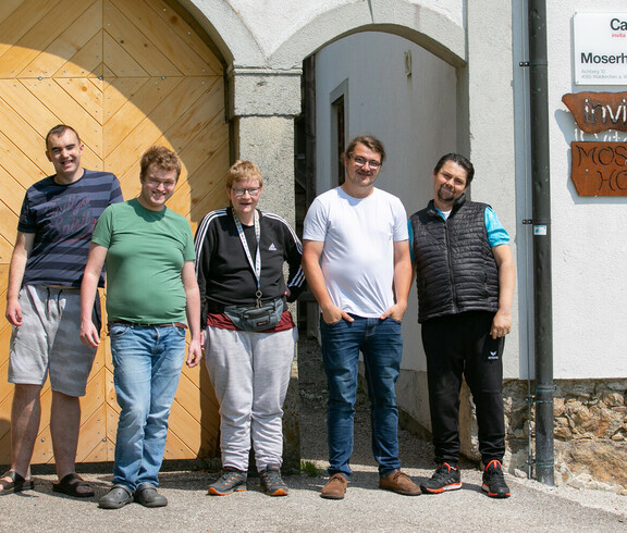 Fünf Männer stehen vor einem hellbraunen Holztor und einer kleineren Tür.