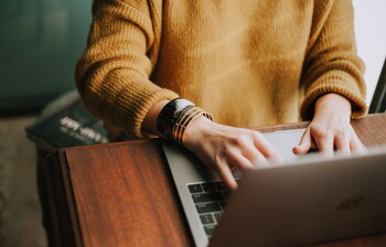 Frau tippt auf der Tastatur eines Laptops, ihre Hände sind im Fokus, ihr Gesicht ist nicht zu sehen