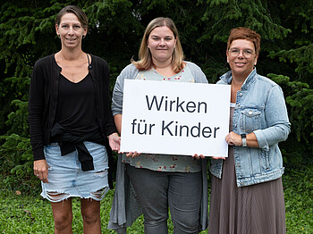 Drei Frauen halten ein Schild mit der Aufschrift: Wirken für Kinder